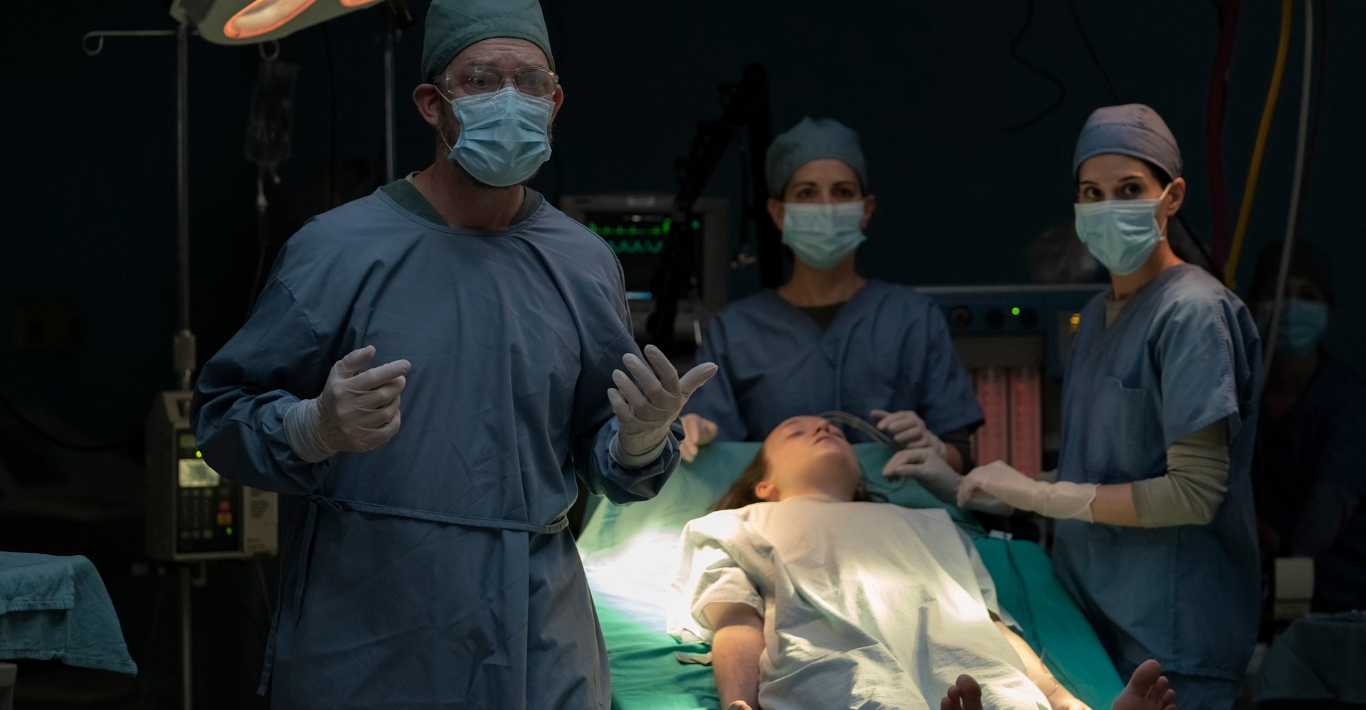 Homens e mulheres em matagais e máscaras ficam em torno de uma mesa cirúrgica segurando a inconsciente Ellie (Bella Ramsey), prestes a sacrificar -a, na última temporada da temporada 1, episódio 9