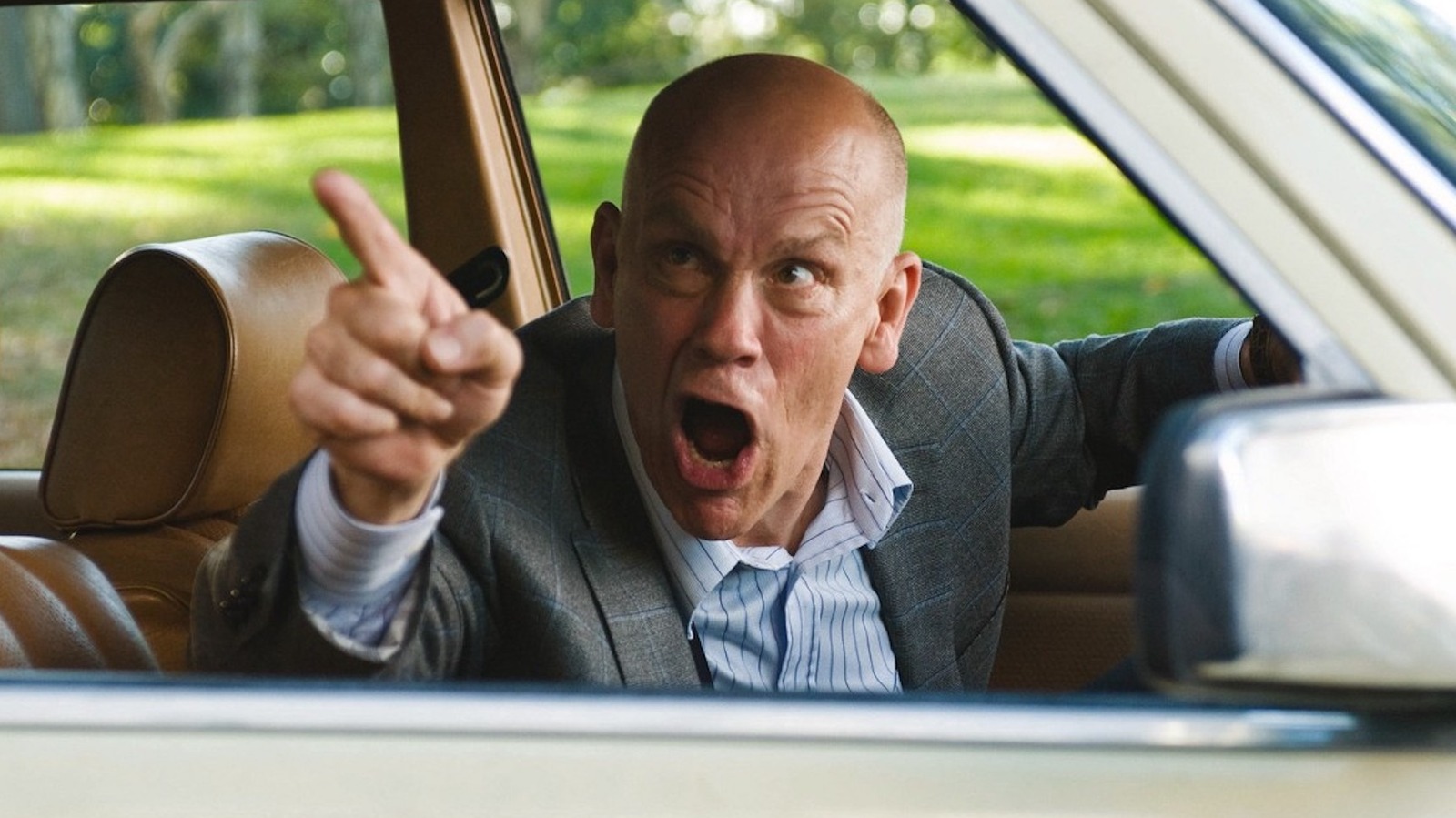John Malkovich sentado em um carro, apontando pela janela e gritando na queima dos irmãos Coen depois de ler