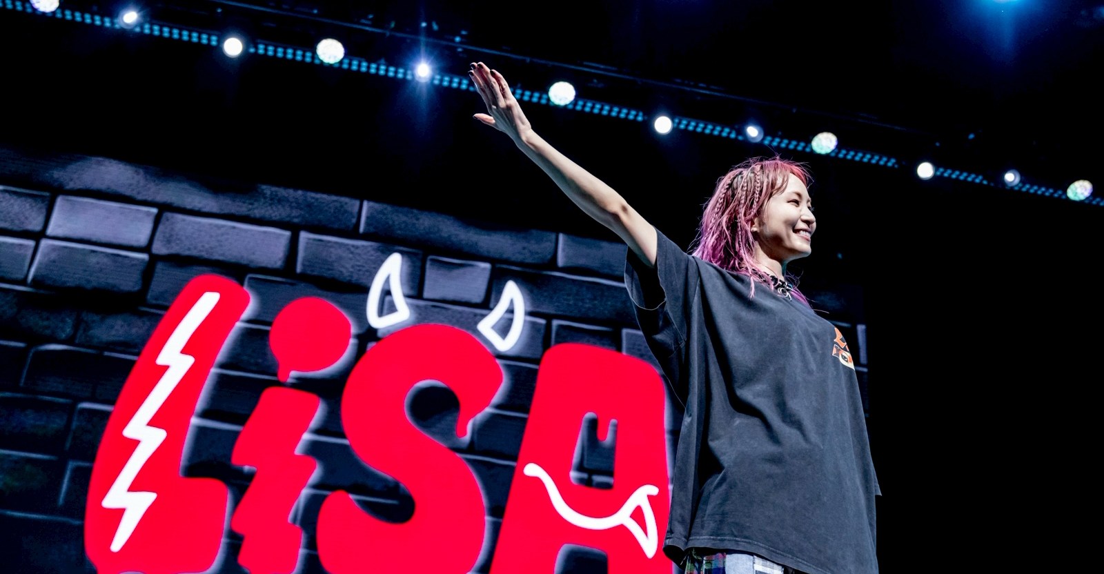O músico do j-pop Lisa, no palco com uma enorme placa vermelha com o nome dela-com pequenos chifres de diabo no 