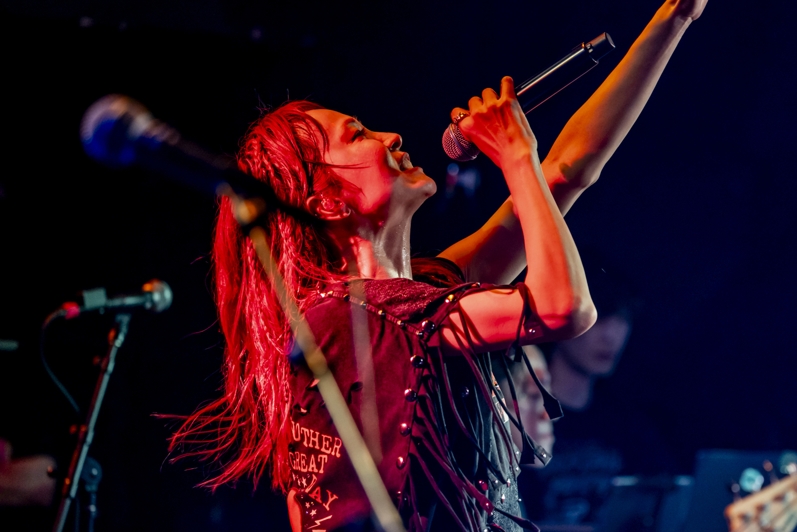 Músico do J-pop Lisa, no palco cantando em um microfone, iluminado em vermelho escuro