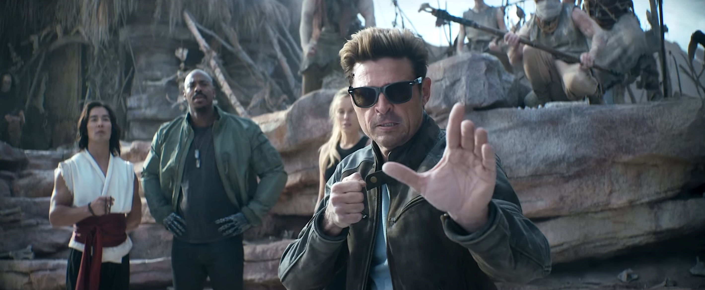 Karl Urban como Johnny Cage atinge uma pose de artes marciais no trailer de Mortal Kombat II como Lui Kang e Jax estão atrás dele no fundo