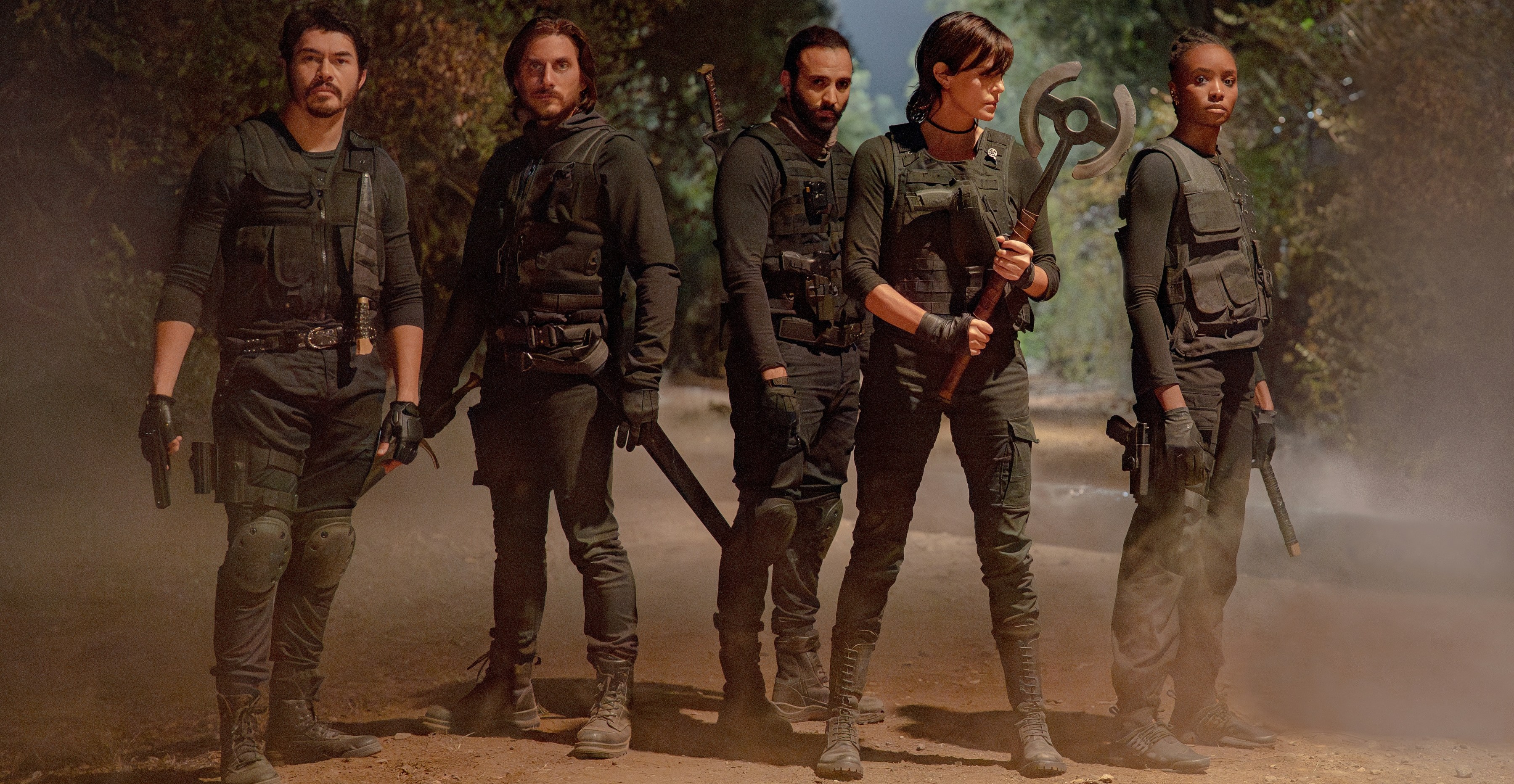 Uma equipe de imortais armados e seus parceiros (interpretados por Henry Golding, Luca Marinelli, Marwan Kenzari, Charlize Theron e Kiki Layne) usando roupas de estilo militar escuro em uma estrada empoeirada no velho guarda 2