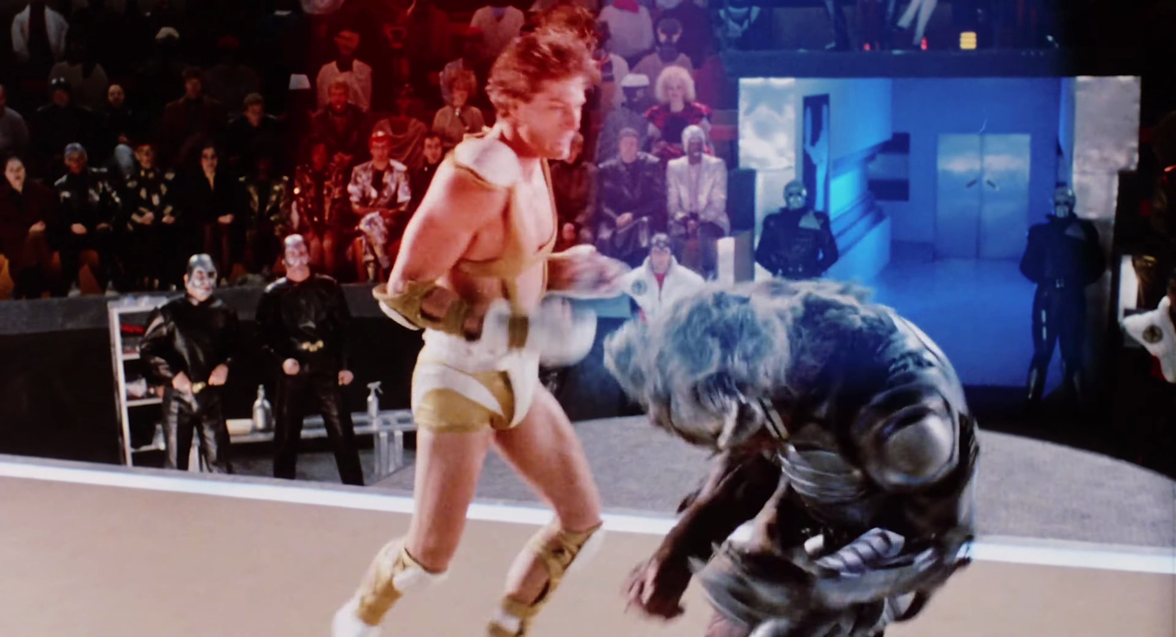 Lutador humano Steve Armstrong (Paul Satterfield), vestindo uma espécie de fralda blindada com alças, leva o anel contra uma espécie de chimpanzé ciborgue na arena de filmes de ficção científica de 1989