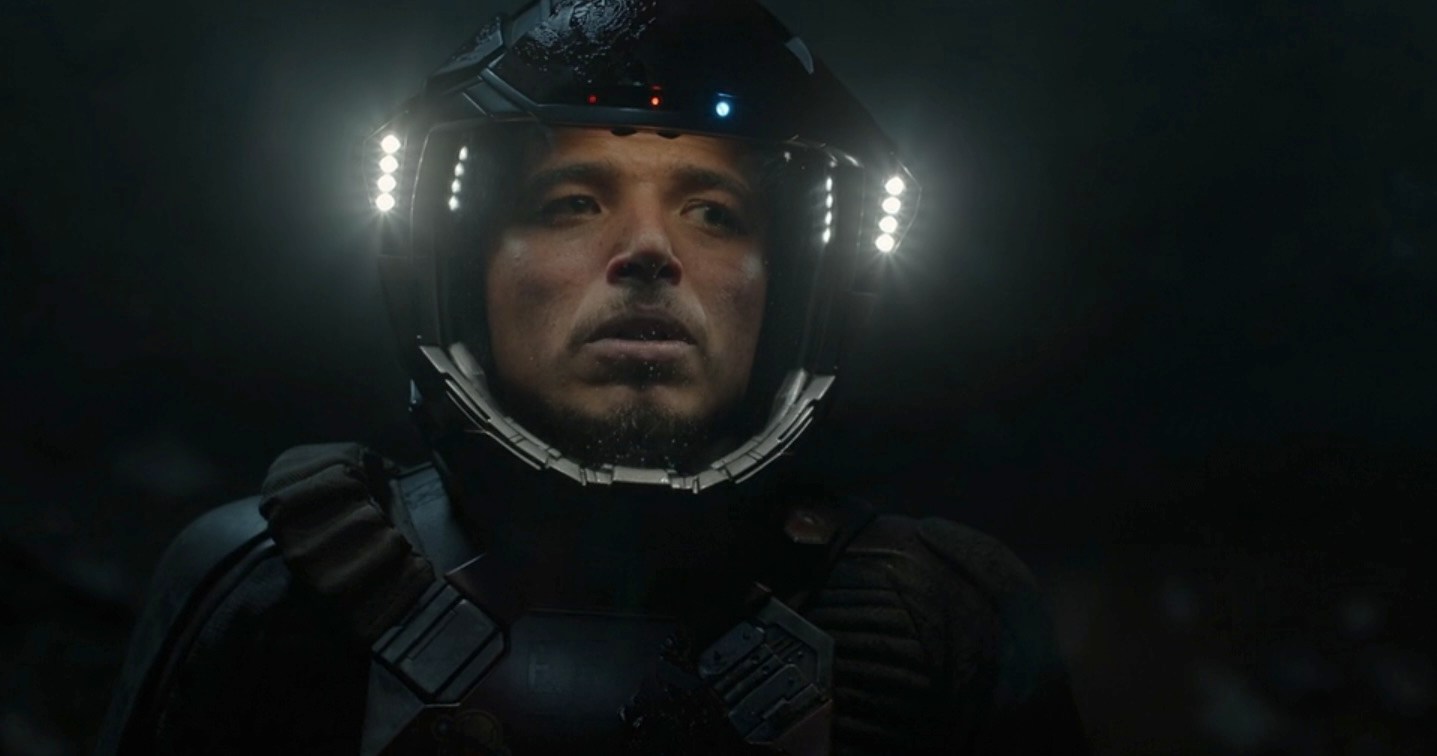 Andy (Anthony Ramos) de longa distância na escuridão usando as luzes do capacete em seu traje espacial