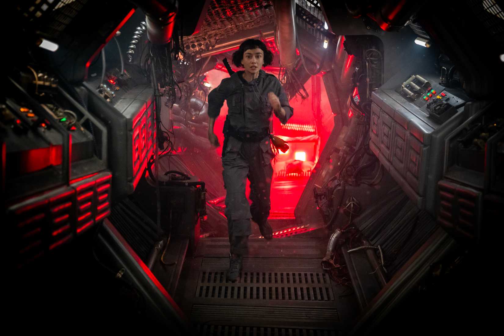Sydney Chandler como Wendy na terra alienígena, correndo por um corredor de nave espacial iluminado por trás com a luz vermelha.
