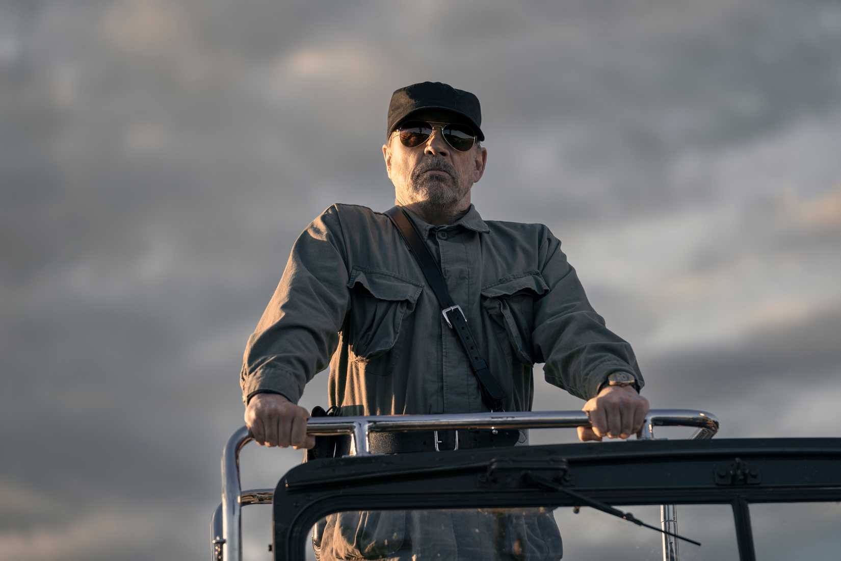 O major (Mark Hamill), um homem de uniforme militar cinza, chapéu preto e óculos de sol opacos, fica na parte de trás de um veículo na longa caminhada