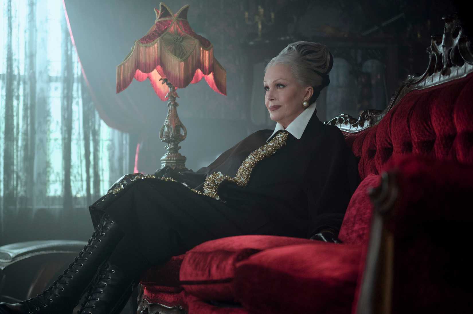 Imagem de quarta -feira com Hester Addams. Ela se senta em um sofá vermelho e exuberante.