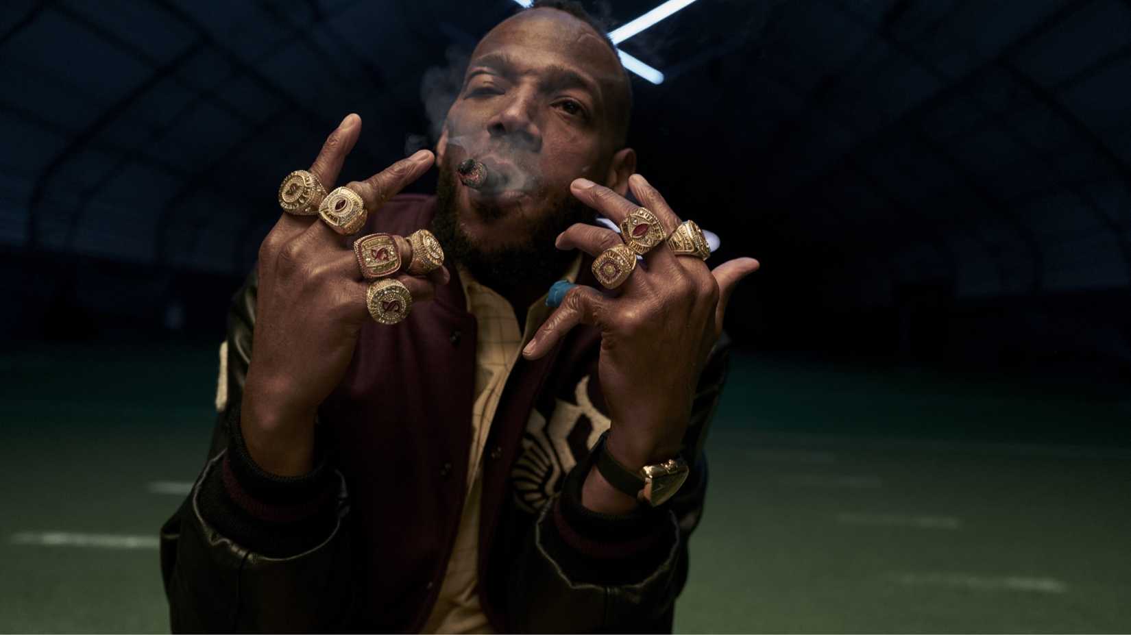 Marlon Wayans como Isaiah White nele, mostrando oito anéis do campeonato da NFL nos dedos na câmera, carrancudia e fumando em um charuto com uma nuvem de fumaça em volta da cabeça