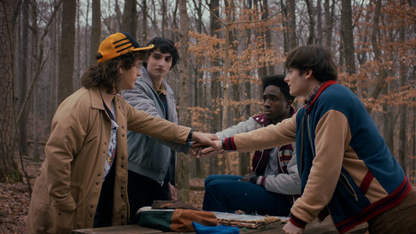 Uma captura de tela da 5ª temporada de Strangerthings, com os quatro protagonistas de mãos dadas na floresta durante um juramento