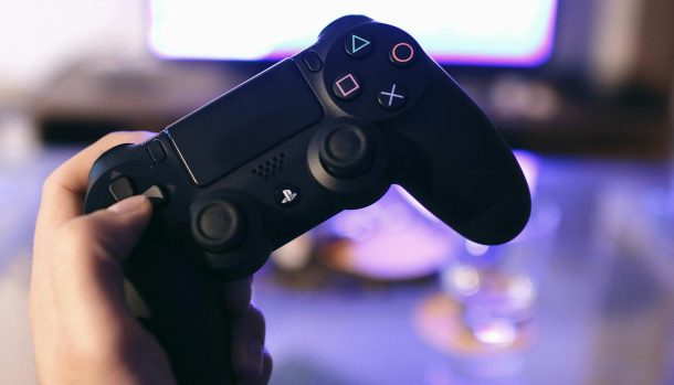 Person holding a gaming controller, blurred screen in background.