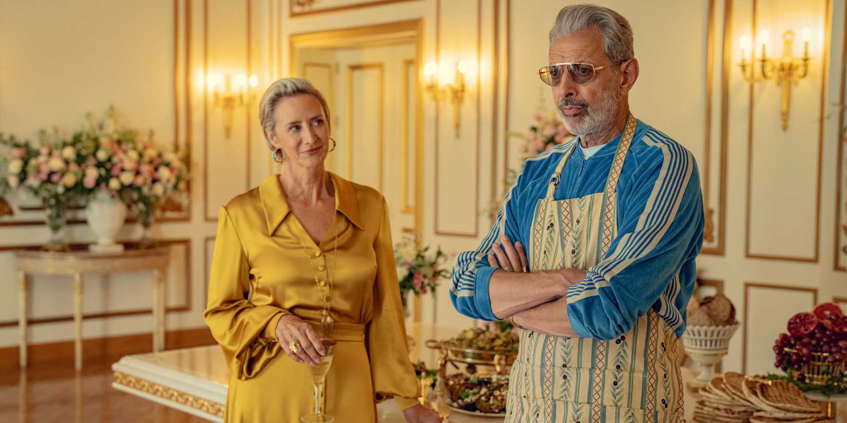 Uma mulher em um vestido dourado e um homem mais velho barbado em um avental no Kaos