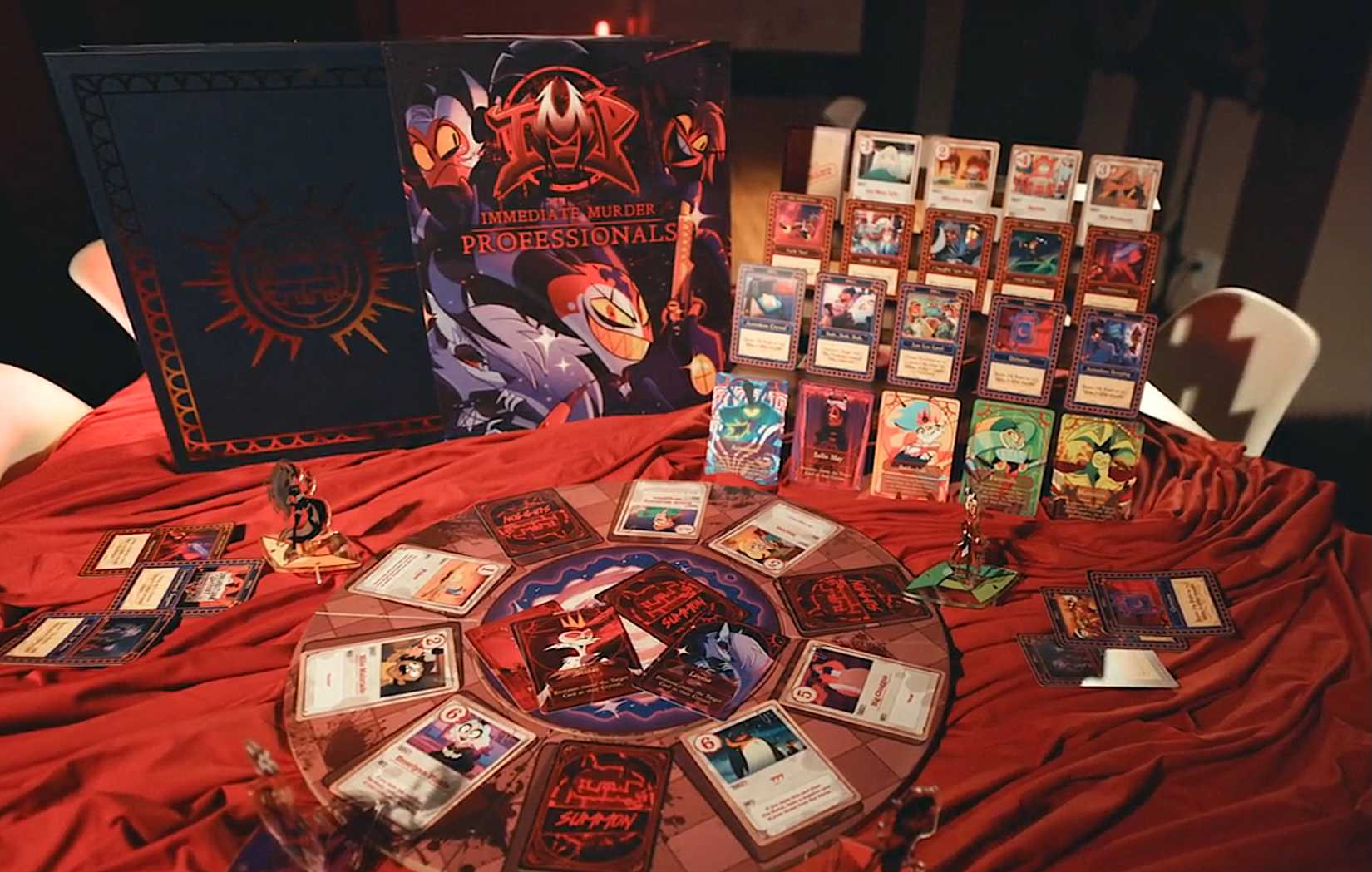 Um layout dos componentes para profissionais de assassinato imediato: um jogo oficial do Boss Helluva, com cartas, standes e uma caixa em uma cortina de tecido vermelho