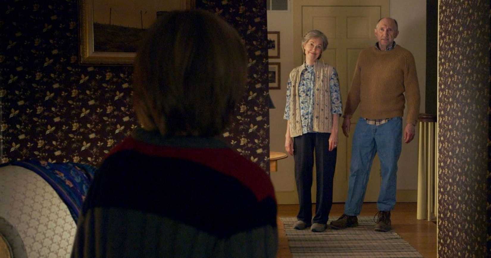 Um garoto, visto pelas costas, olha para seus avós parados na porta de uma cena do filme The Visit. 