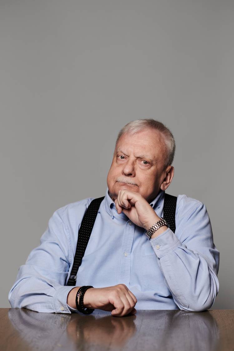 O autor Witcher Andrzej Sapkowski senta -se com o queixo na mão na frente de um cenário cinza