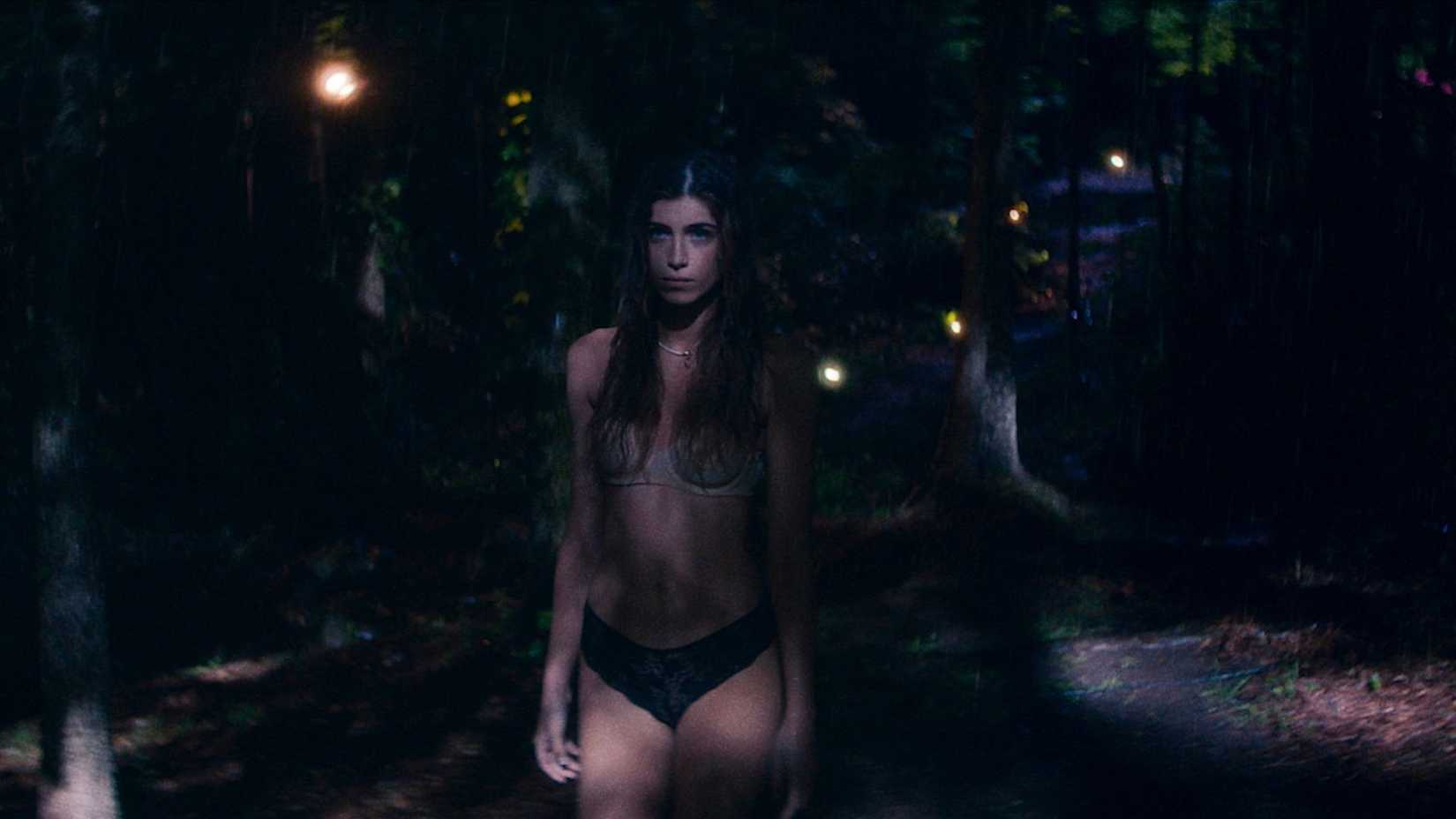 Andra Nechita, uma mulher de cabelos escuros em lingerie rendada, fica no escuro do lado de fora em Bone Lake.