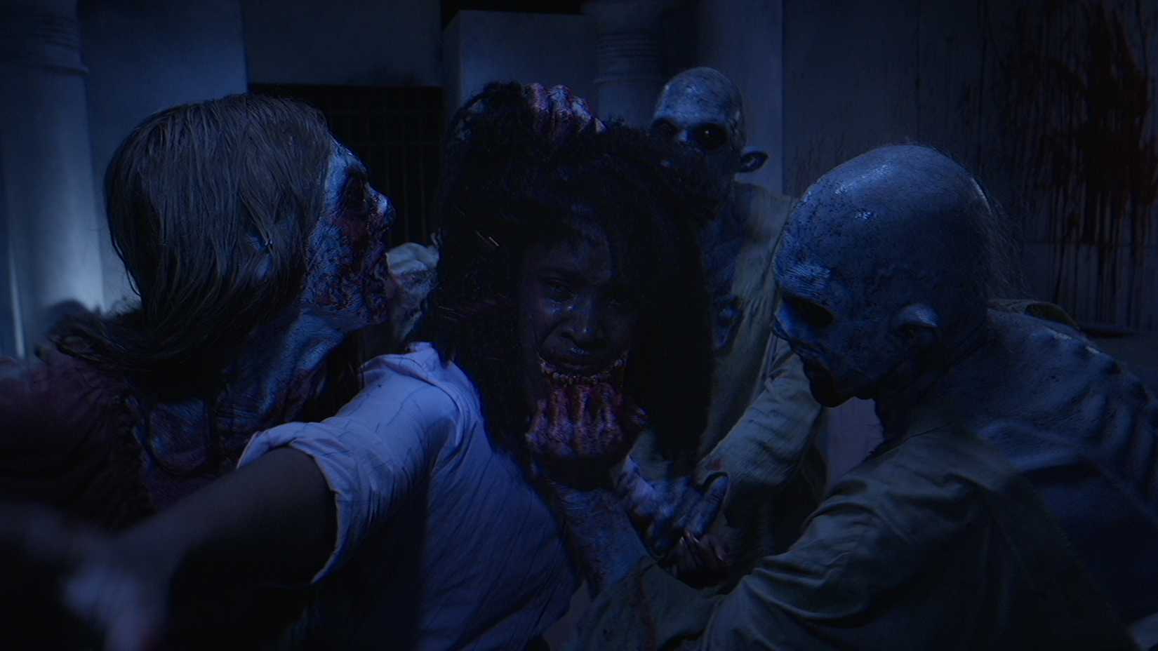 Duas figuras macabras e manchadas de sangue rasgam na face de um adolescente chorando em um corredor escuro como um terceiro esconderias para trás no curto do Halloween V/H/H "Home Haunt"