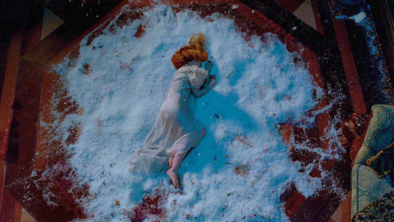 Captura de tela do Pico Carmesim. Mostra Edith, de vestido branco, no chão onde está um monte de neve. Ela está descalça e ferida.