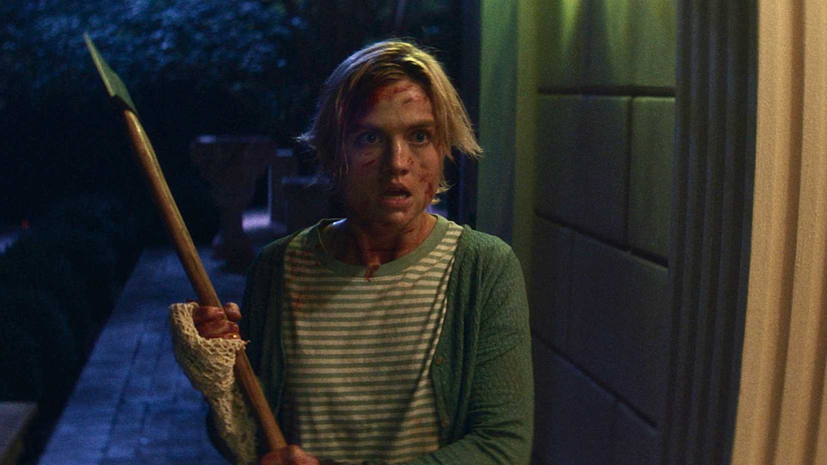 Uma mulher loira com um rosto ensanguentado, segurando um machado encara a tela, de boca aberta, em Bone Lake