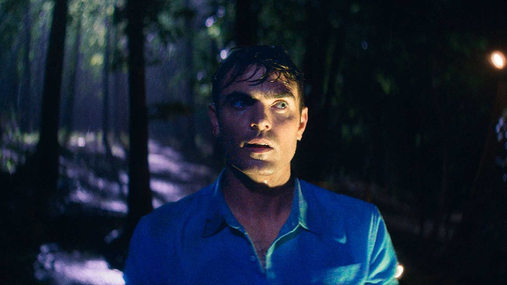 Um parado de Bone Lake mostrando um homem molhado cercado por uma floresta escura. Ele parece nervoso.