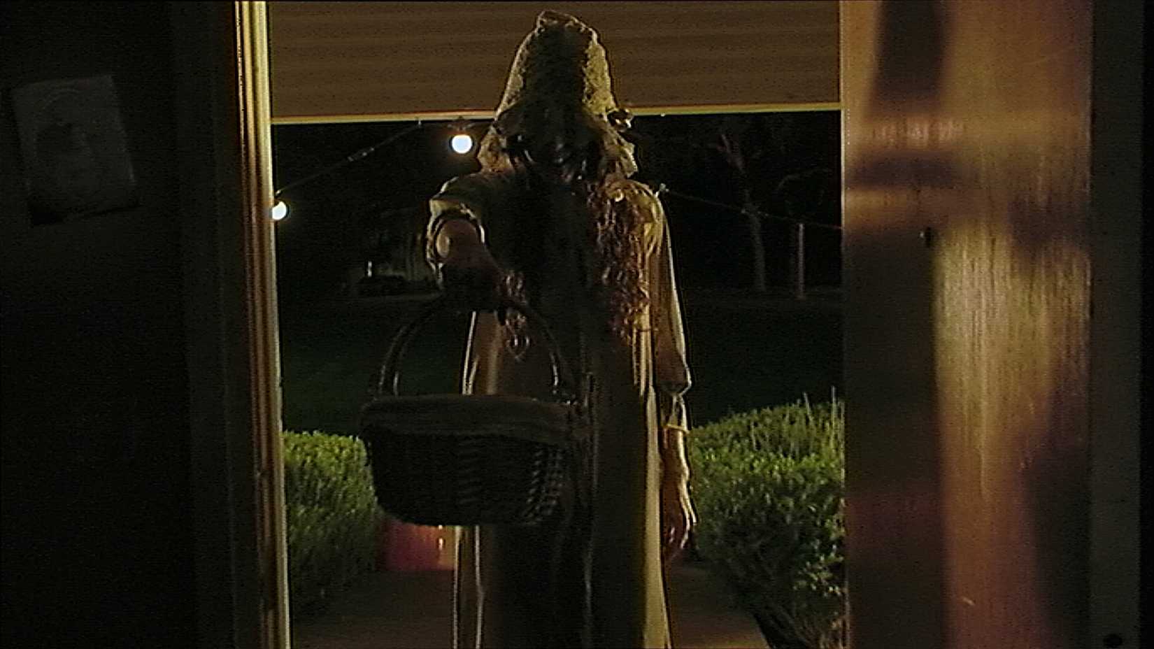 Uma bruxa assustadora com um sorriso assustador bloqueia uma porta aberta de uma casa no short V/H/S Halloween "Coochie Coochie COO"