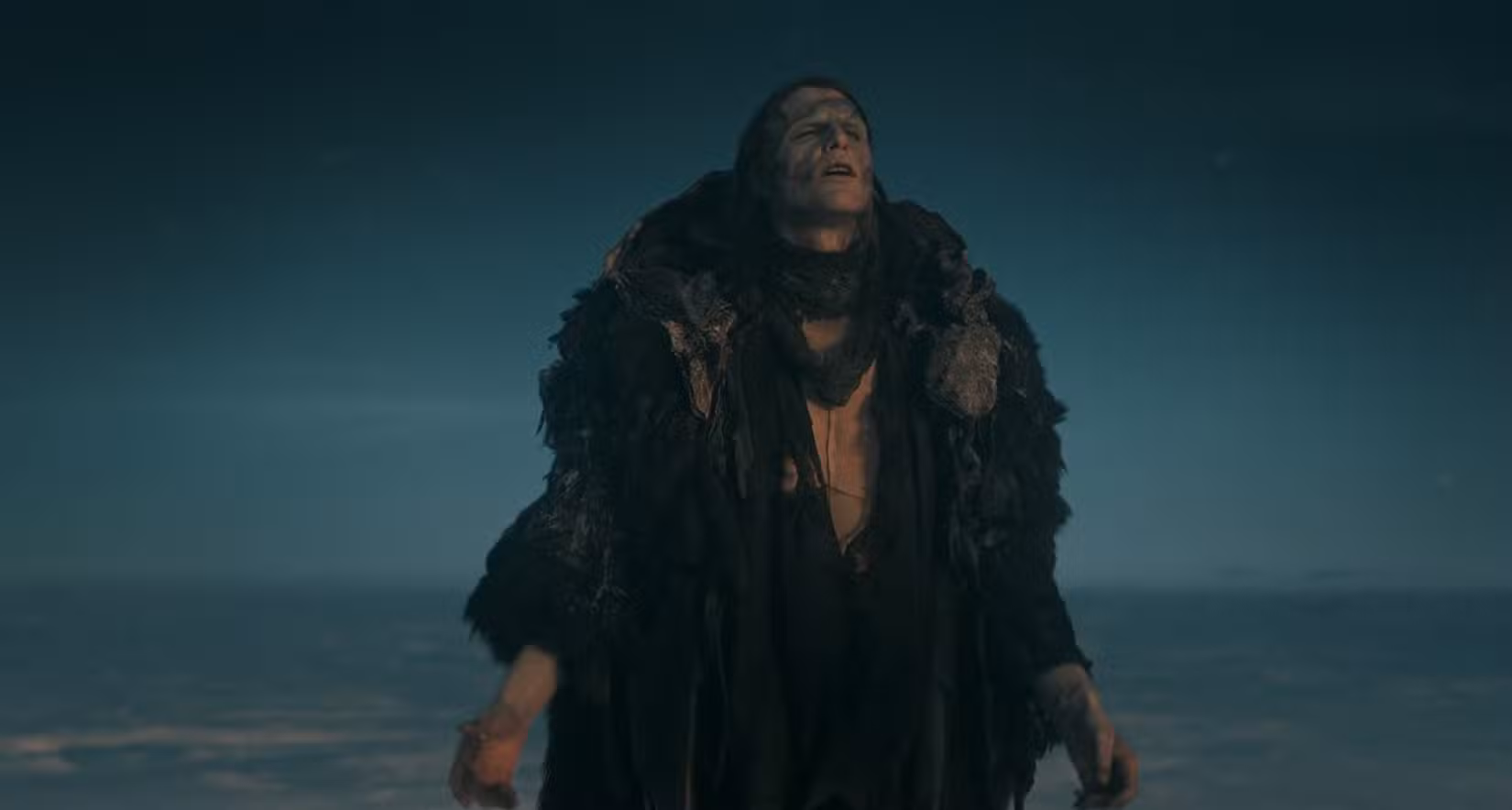 A Criatura, interpretada por Jacob Elordi, tira a capa e fecha os olhos diante da paisagem congelada em uma cena do filme Frankenstein de Guillermo del Toro