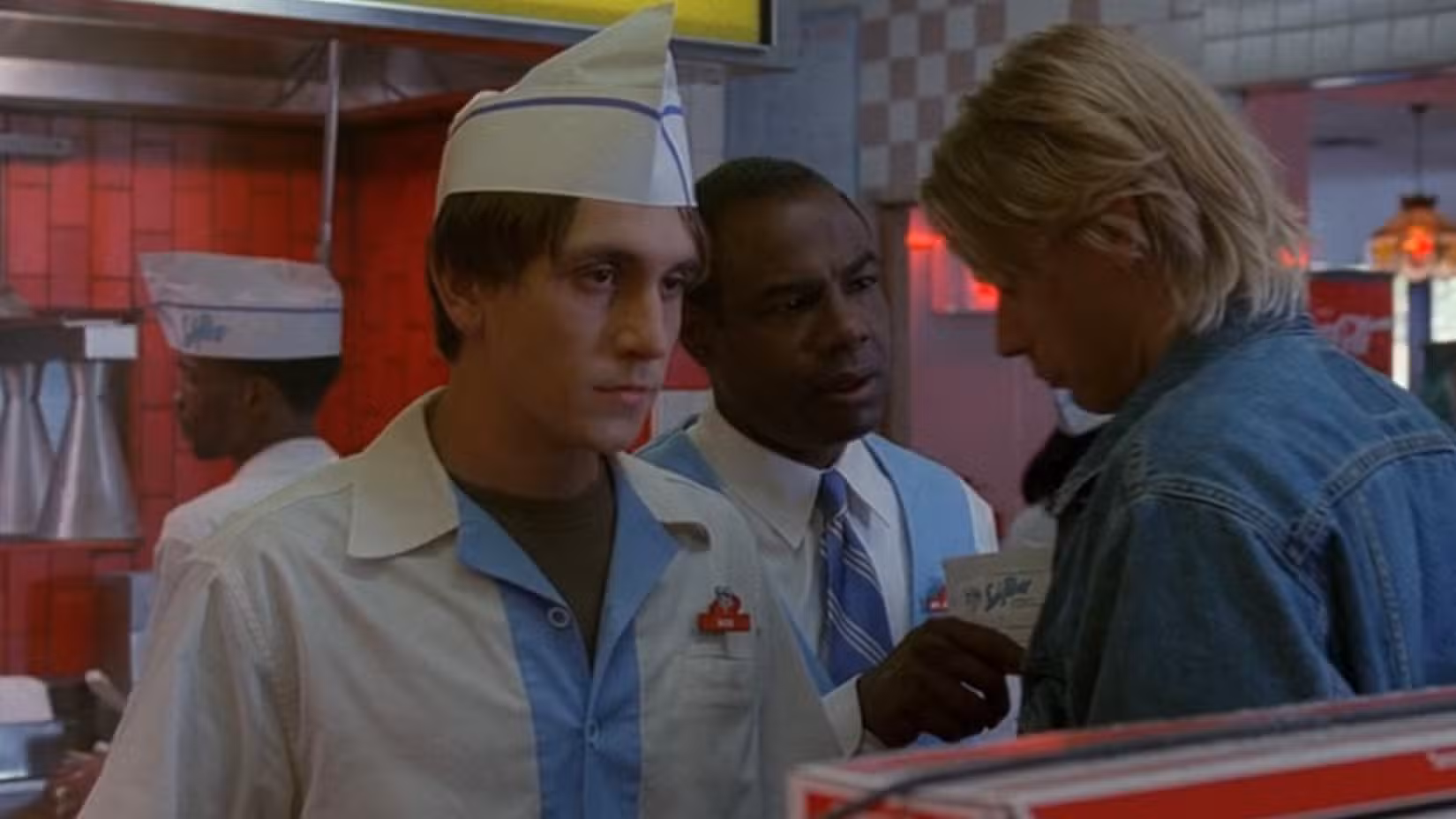 Um trabalhador de fast-food (Chad Donella) parece chateado enquanto seus colegas de trabalho discutem no episódio de Arquivo X "Com fome"