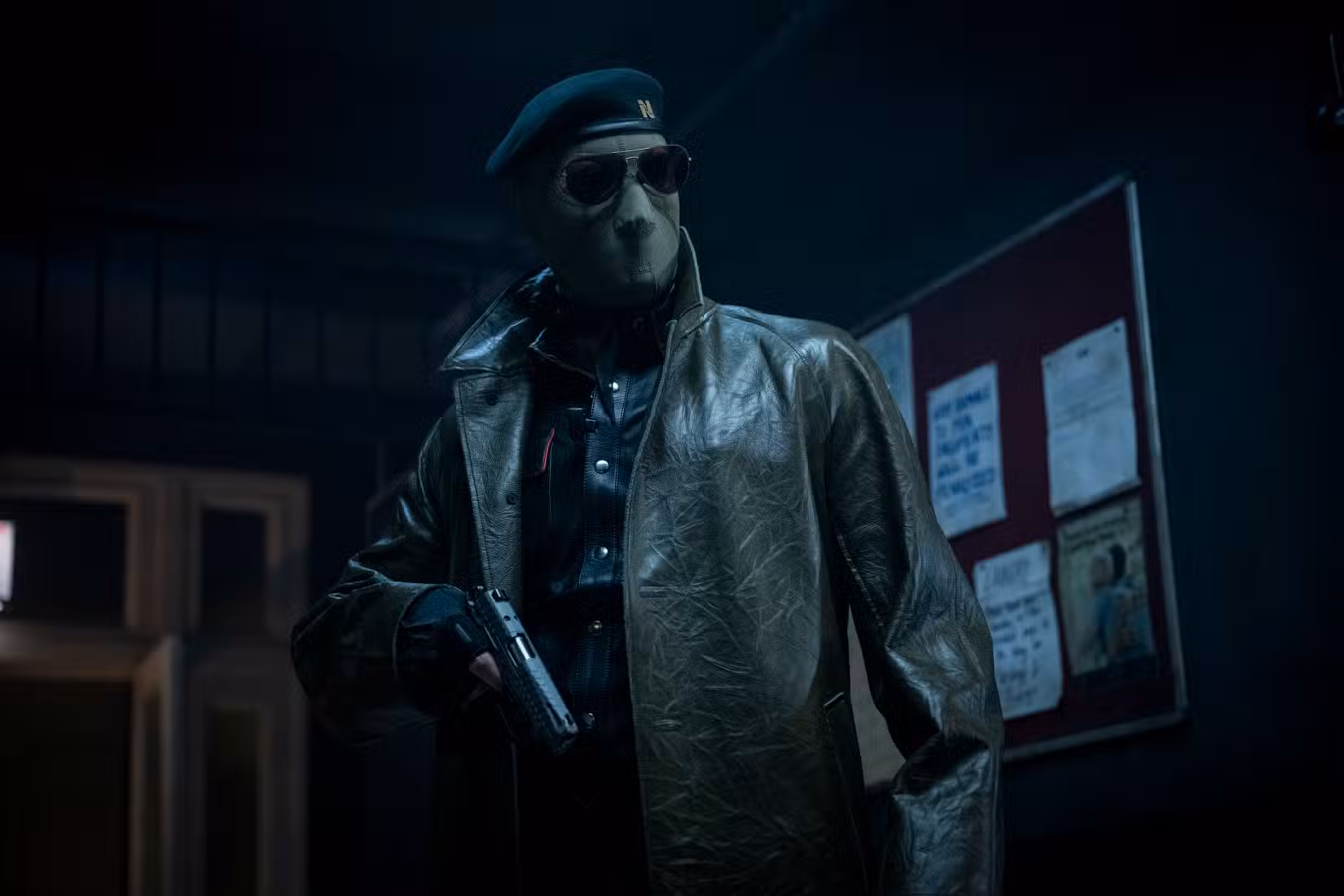 Lee Pace (embora você não possa dizer se é ele, ou alguém realmente) usa uma máscara facial estilo ICE, óculos escuros e jaqueta de couro e segura uma arma no 2025 Running Man