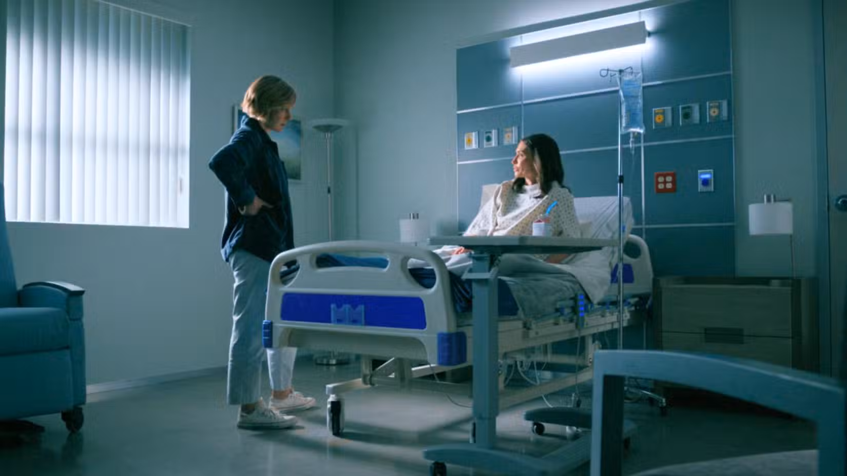 Uma captura de tela do episódio 4 de Pluribus apresentando Rhea Seehorn como Carol Sturka e Karolina Wydra como Zosia. Carol está visitando Zosia, que está deitada em uma cama de hospital.