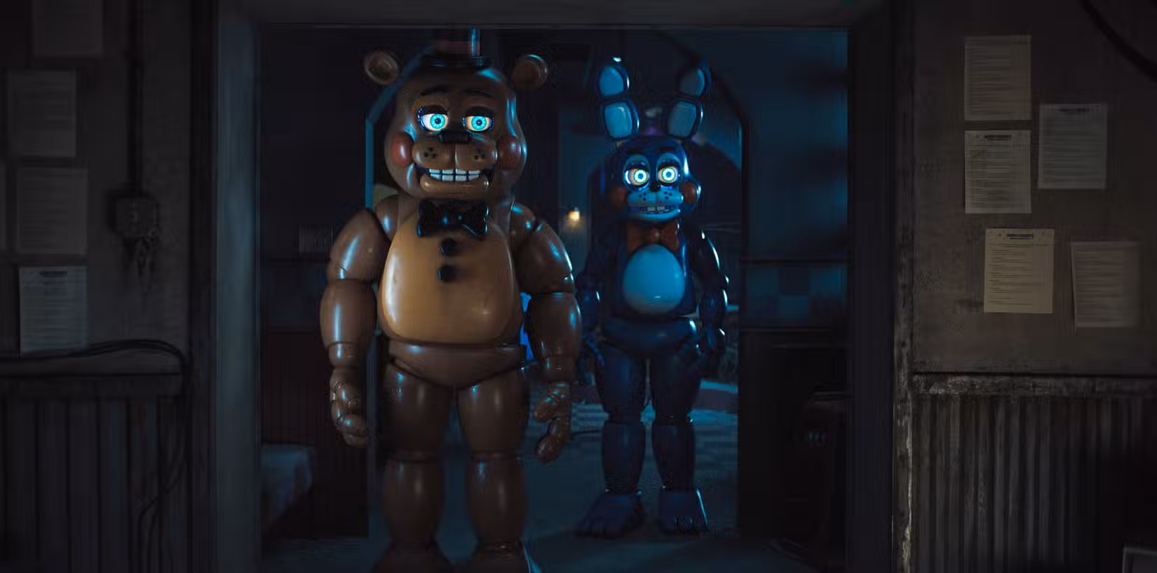Dois robôs animatrônicos assustadoramente sorridentes, um urso marrom e um coelho azul, estão em um corredor escuro, com os olhos brilhando, em Five Nights at Freddy's 2