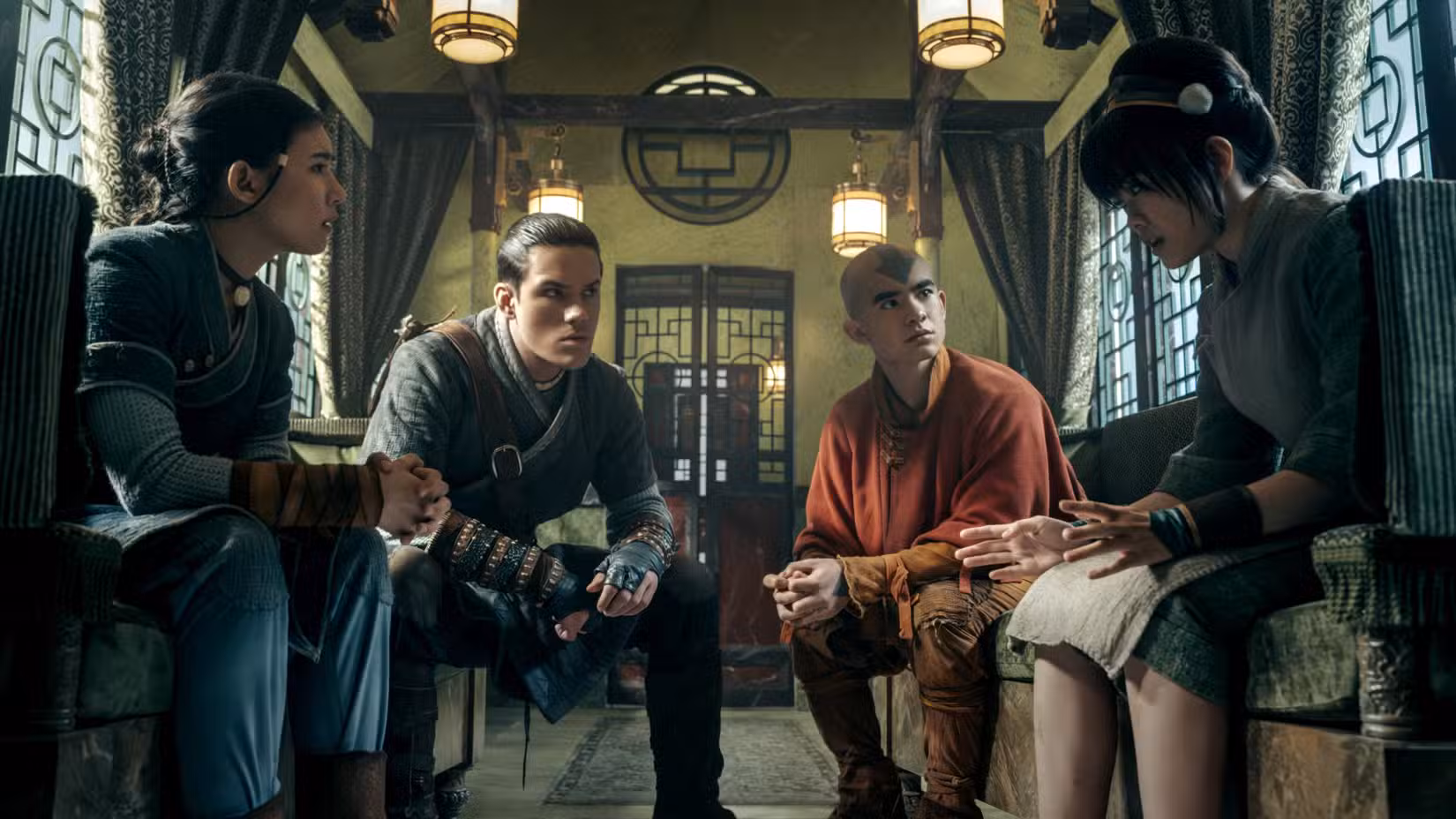 Katara (Kiawentiio), Sokka (Ian Ousley), Aang (Gordon Cormier) e Toph (Miya Cech) sentam-se em um prédio da Nação da Terra em Avatar: O Último Mestre do Ar, temporada 2