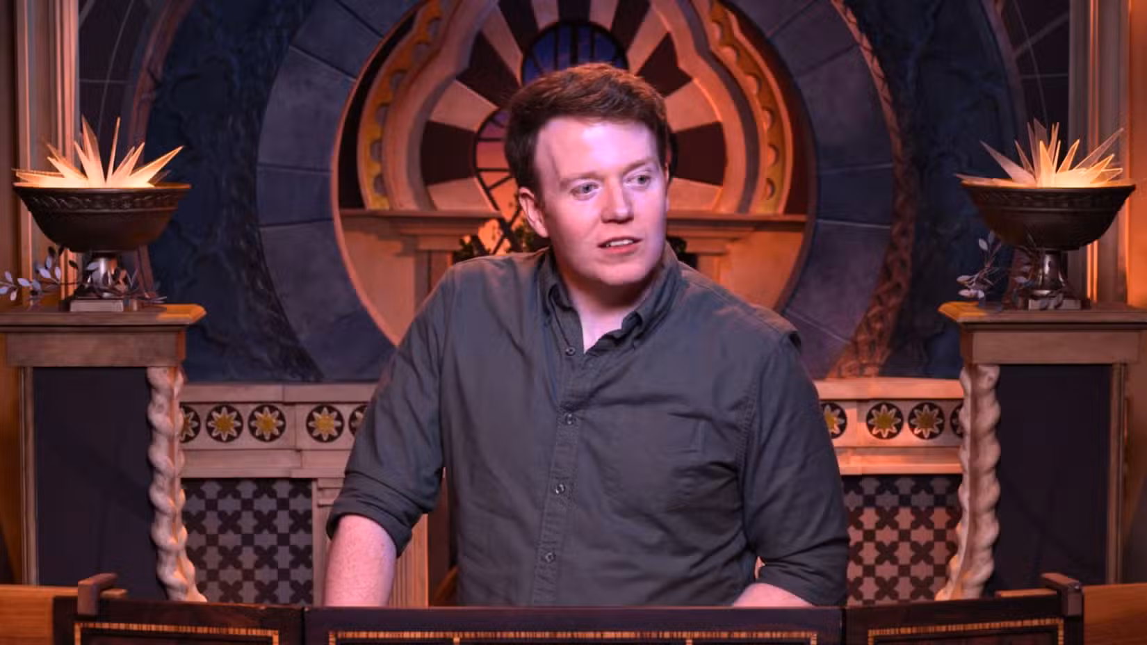 Uma imagem de Brennan Lee Mulligan do episódio 9 do Critical Role Cooldown. Ele veste uma camisa cinza e fica atrás de uma tela DM.