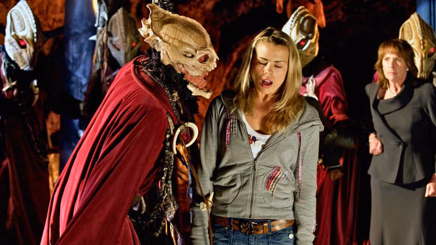 Uma imagem do especial de Doctor Who de 2005, The Christmas Invasion. Um alienígena com uma capa vermelha e uma cabeça em forma de vagem grita com Billie Piper como Rose Tyler. Ela está vestida com jeans e uma jaqueta cinza. Eles estão cercados por outros alienígenas. 