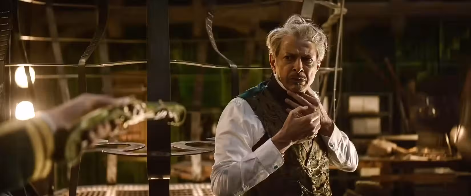 O Mágico de Oz (Jeff Goldblum) parece nervoso enquanto é mantido sob a mira de uma arma por uma figura fora da tela em Wicked: For Good
