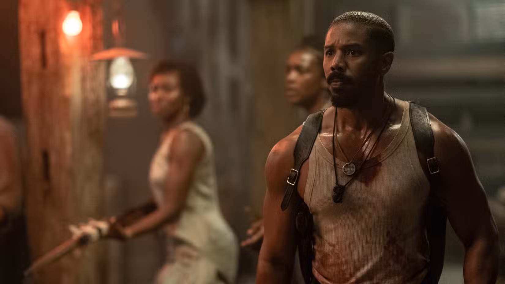 Michael B. Jordan, suado e com uma camiseta sem mangas manchada de sangue, parece preocupado e abatido em Sinners, de Ryan Coogler