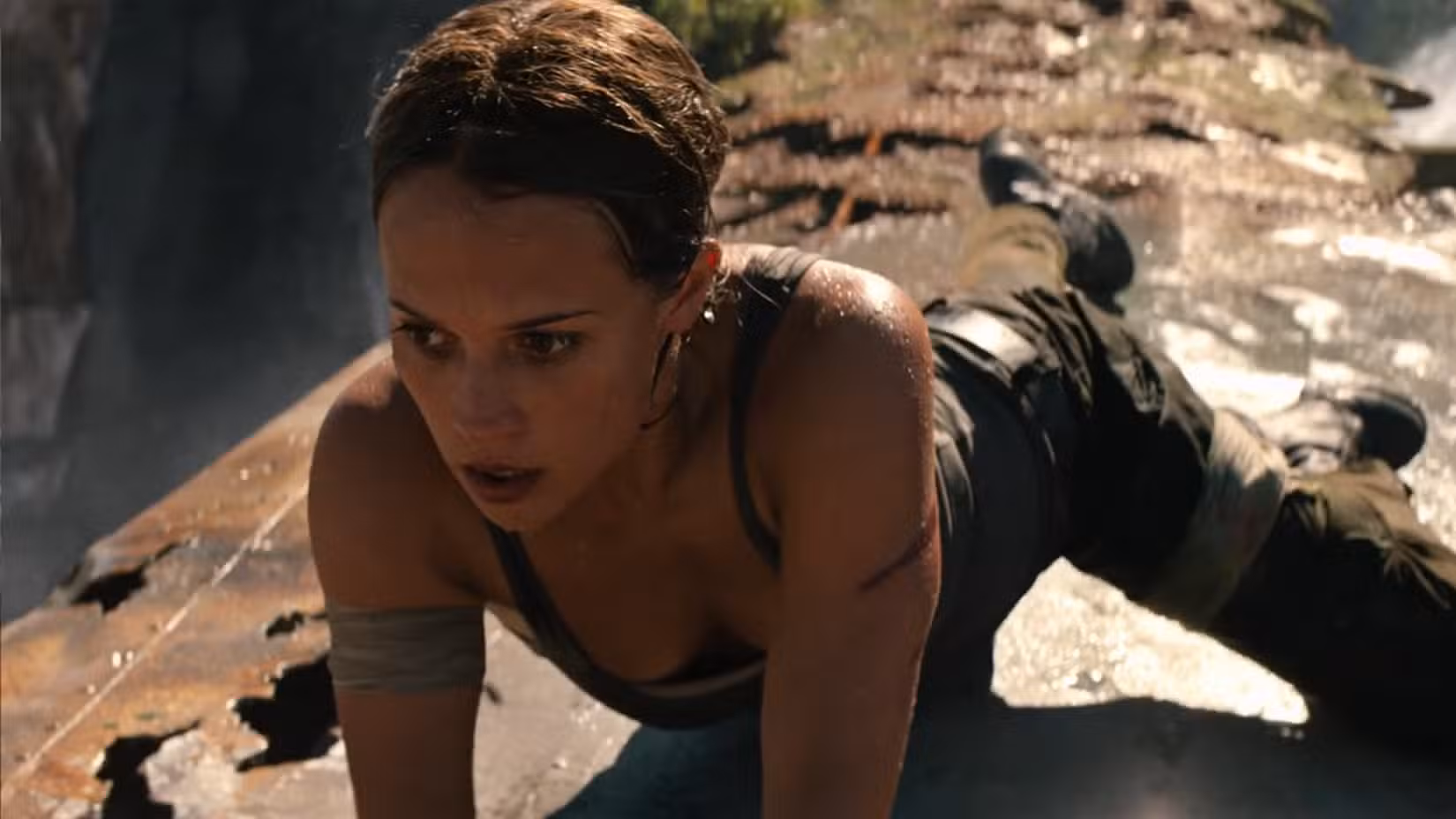 Lara Croft (Alicia Vikander) se equilibra na asa enferrujada de um avião pousado acima de uma cachoeira, mostrada aqui em close, em cena de Tomb Raider (2018)