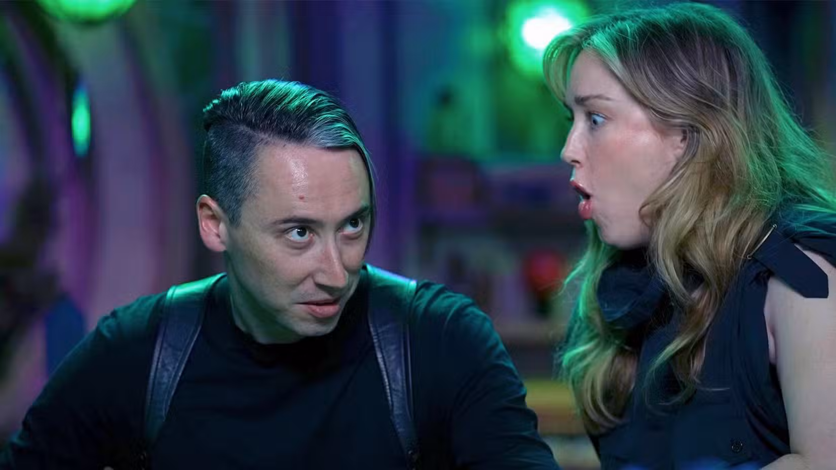 Uma imagem da Critical Role apresentando Alex Ward e Ashley Johnson. Alex tem uma expressão séria no rosto, todo vestido de preto. Ashley, ao lado dele, faz uma cara de choque. 