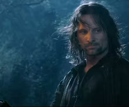 Um Aragorn enlameado está em uma floresta, segurando uma tocha acesa em A Sociedade do Anel.