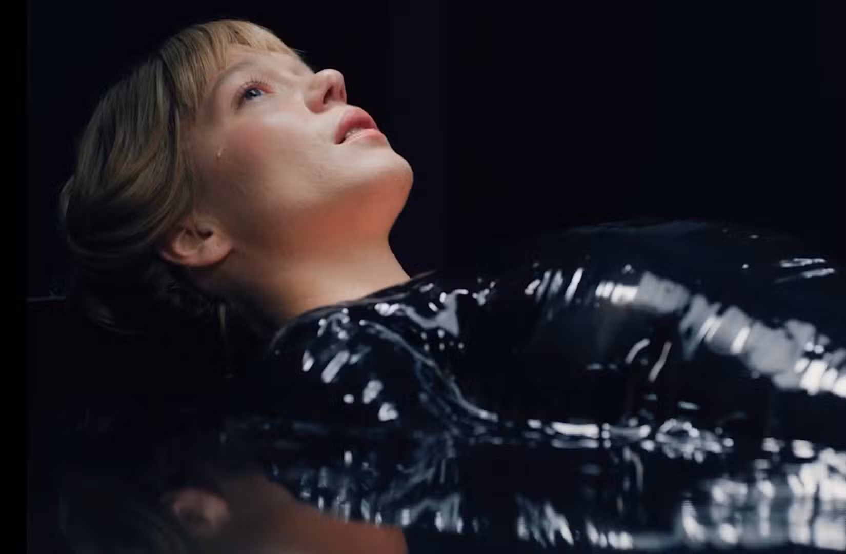 Gabrielle (Léa Seydoux), uma jovem pálida vestida de vinil preto, está deitada de costas olhando para cima com uma lágrima escorrendo pelo rosto em A Besta