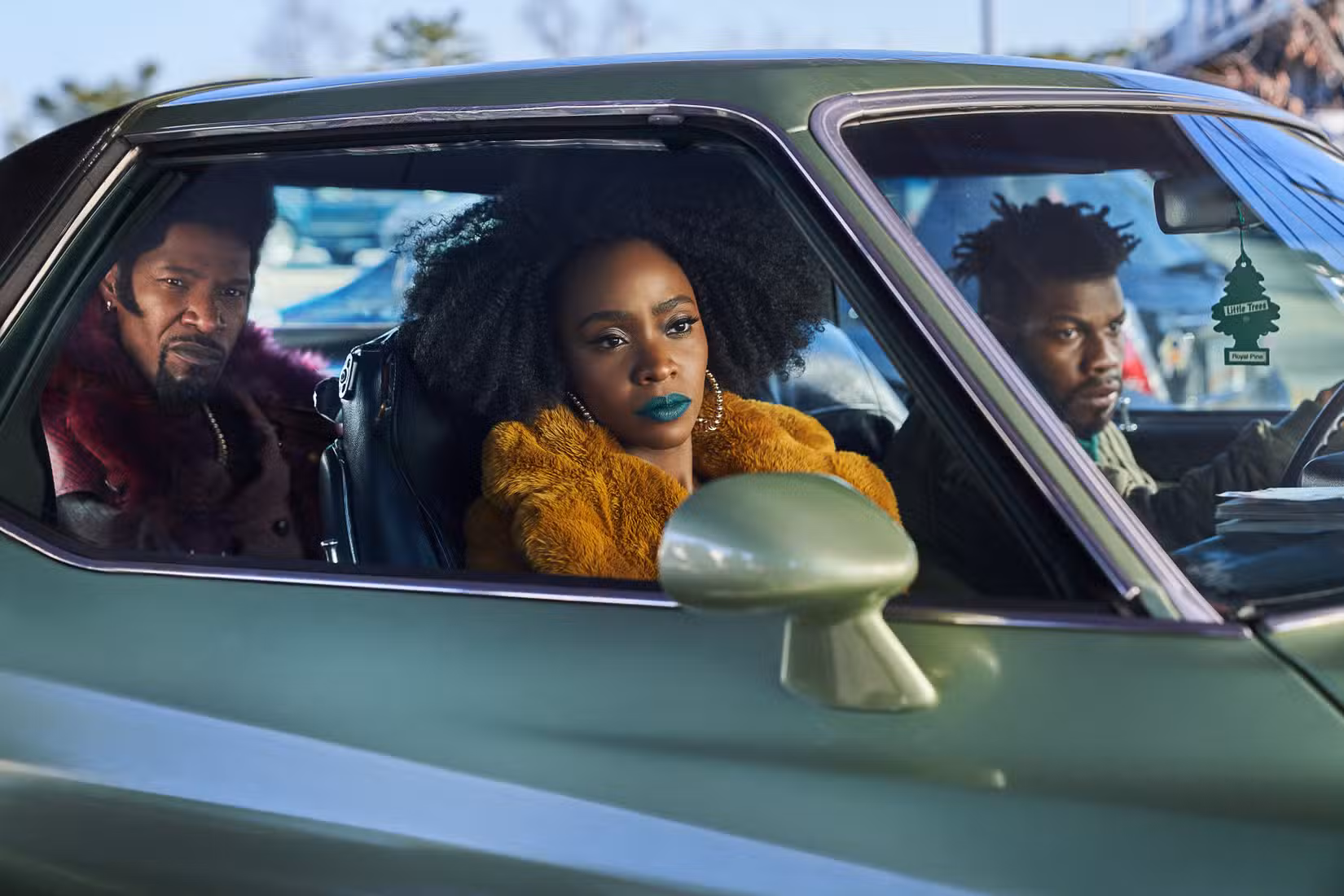 Jamie Foxx como Slick Charles, Teyonah Parris como Yo-Yo e John Boyega como Fontaine, todos sentados em um carro em They Cloned Tyrone.