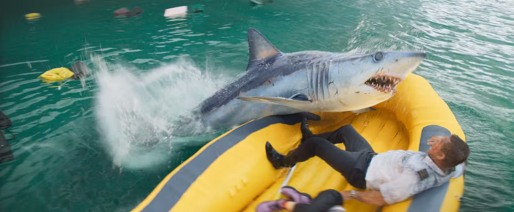 Em uma cena aérea do filme sobre tubarões de 2026, Deep Water, um tubarão se joga em um bote salva-vidas amarelo segurando um piloto de avião interpretado por Aaron Eckhart. 
