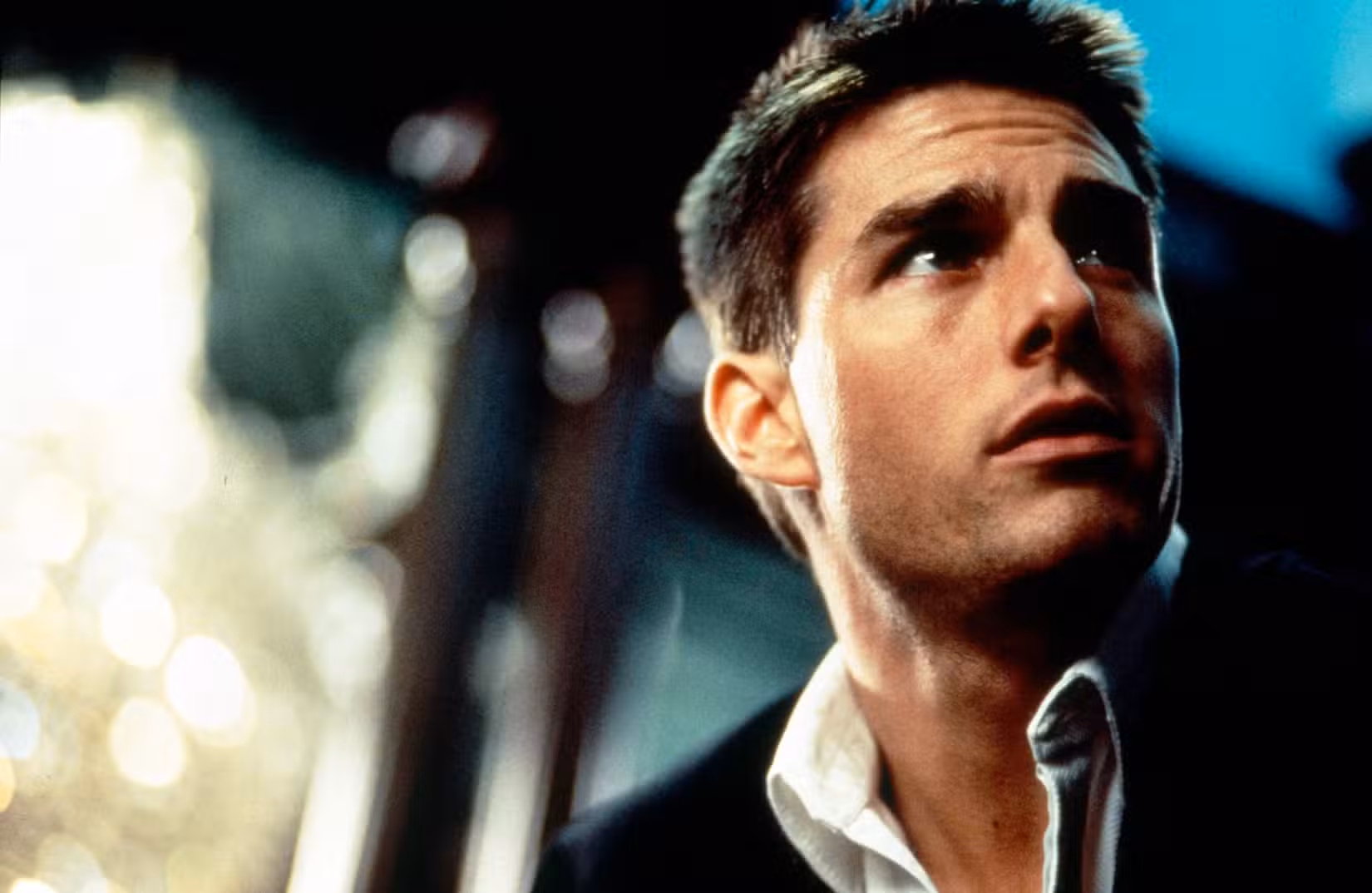 Tom Cruise com camisa de gola aberta, olhando para cima
