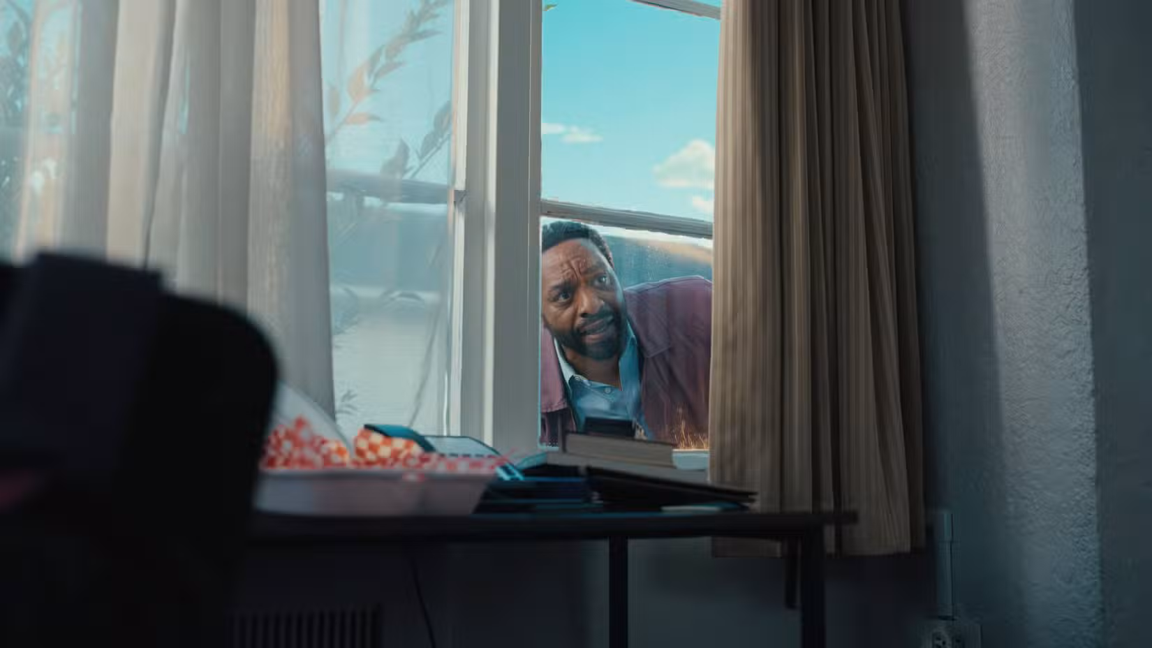 Clark (Chiwetel Ejiofor) espia pela janela com cortinas de uma casa em Backrooms