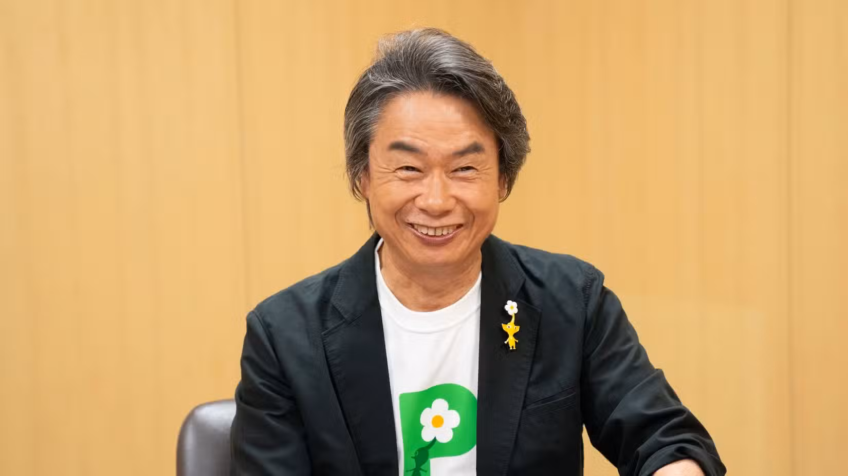 Uma fotografia de Shigeru Miyamoto da Nintendo vestindo uma camiseta e broche Pikmin