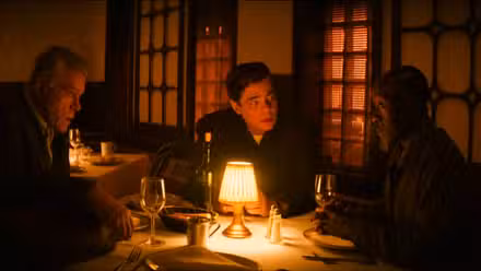 Ray Liotta, Don Cheadle e Benicio del Toro sentam-se ao redor de uma mesa, com as bordas da imagem distorcidas por uma lente olho de peixe, em cena de No Sudden Move 