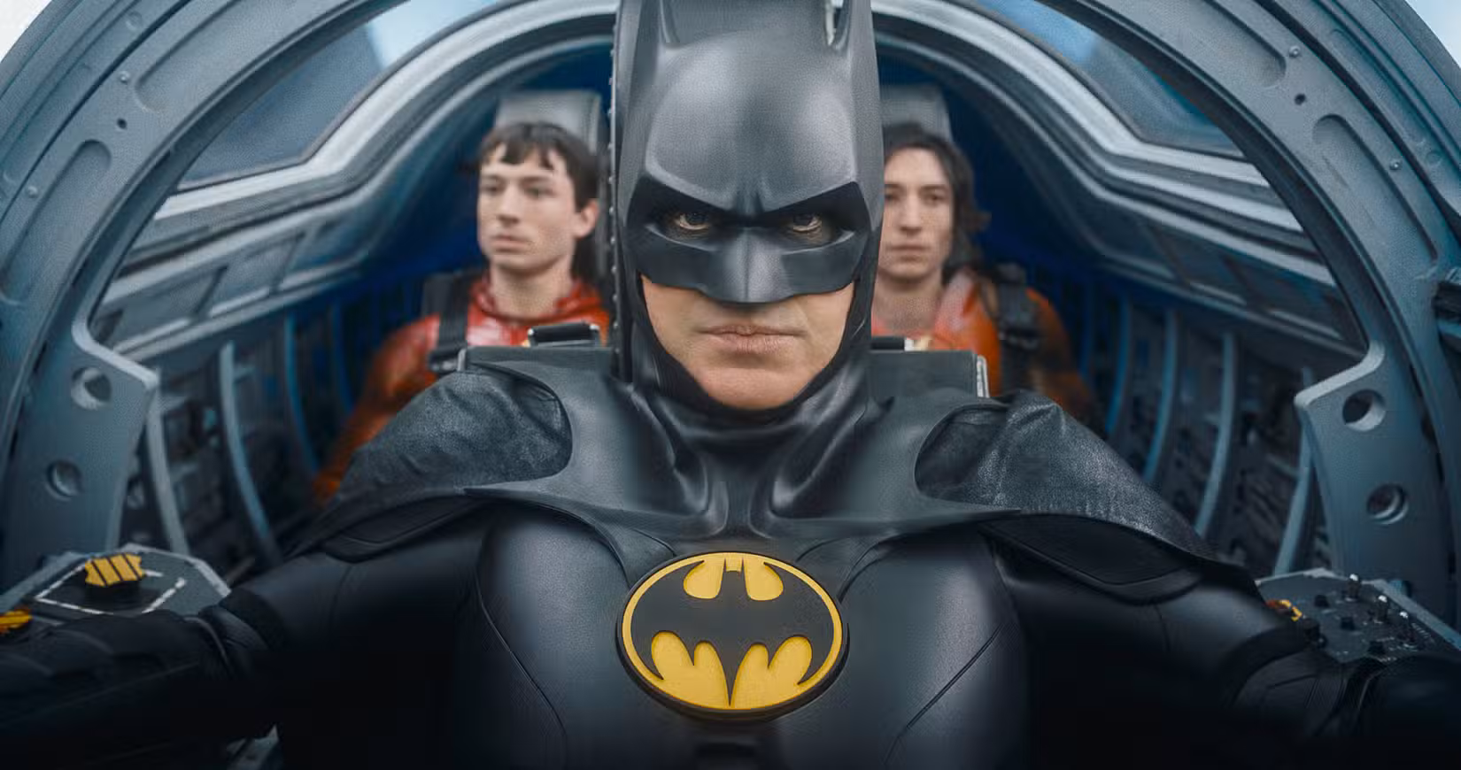 (LR) Ezra Miller como The Flash, Michael Keaton como Batman e Ezra Miller como The Flash em The Flash. Eles estão na cabine apertada do Batwing, com Batman no assento do piloto e os dois Flashes sentados um ao lado do outro atrás dele.
