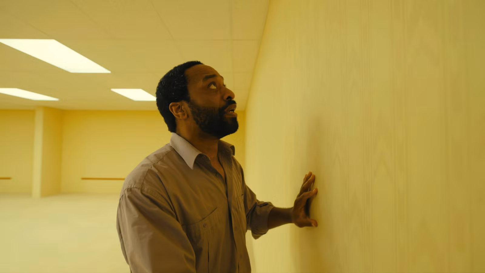 Clark (Chiwetel Ejiofor) passa as mãos por uma parede amarela em Backrooms