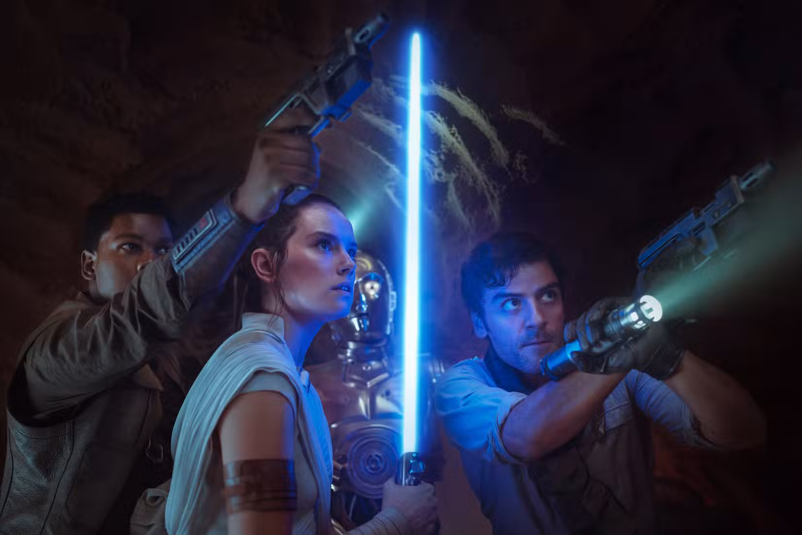 Finn apontando sua arma para cima, Rey segurando seu sabre de luz azul para cima e Poe apontando uma arma e uma lanterna para cima, com C-3PO em pé atrás deles, em Star Wars: The Rise of Skywalker