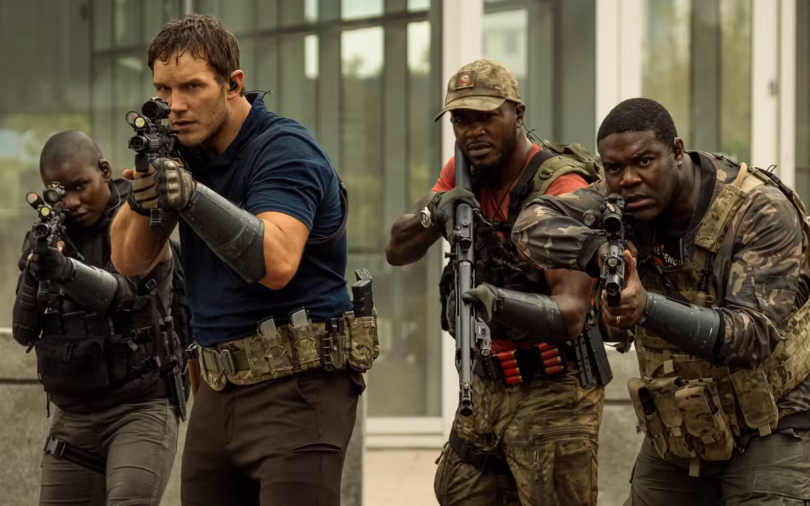 Chris Pratt está significativamente à frente de um pequeno grupo de soldados armados e vestindo camuflagem, todos negros, exceto ele