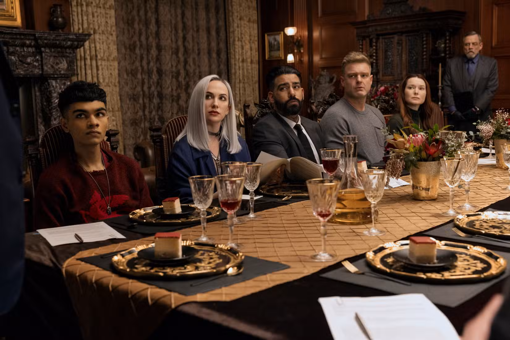 Sauriyan Sapkota, Kate Siegel, Rahul Kohli, Matt Biedel e Samantha Sloyan sentam-se ao redor de uma mesa enquanto Mark Hamill está atrás deles em Fall of the House of Usher.