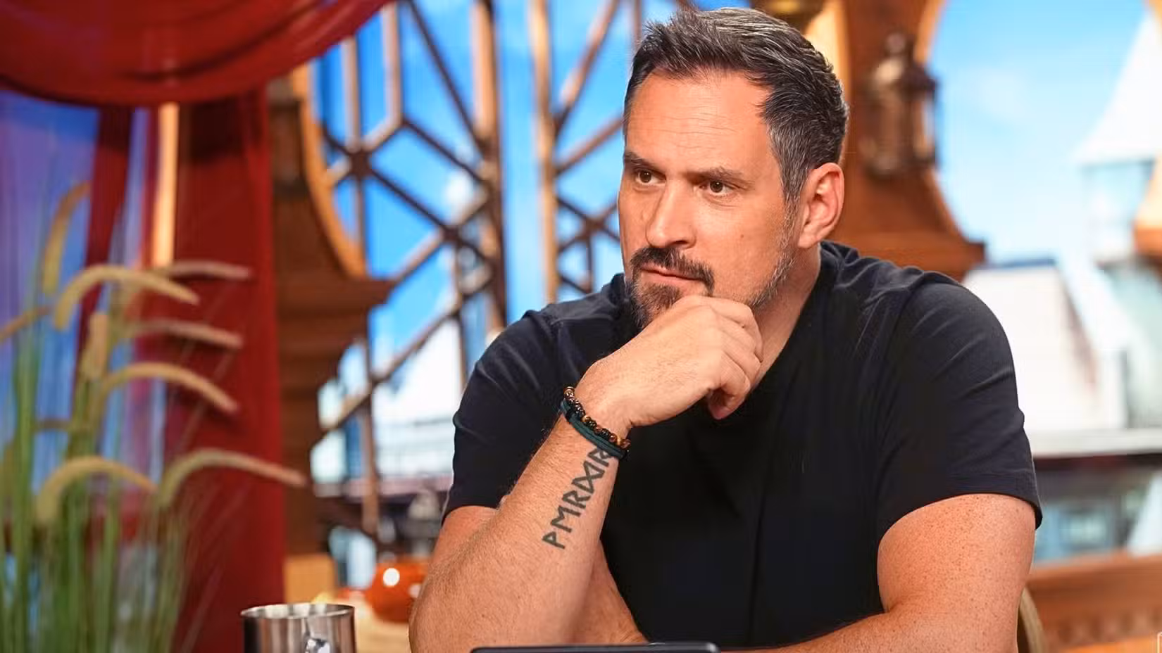 Travis Willingham, da Critical Role, está sentado a uma mesa, parecendo sério.